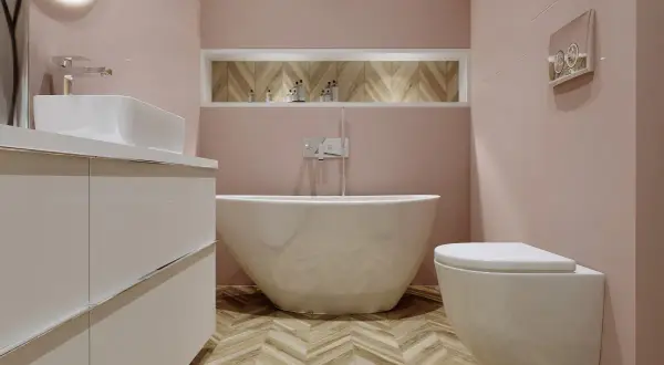 Elegancka łazienka z wolnostojącą wanną i baterią wannową. Jasnoróżowe ściany, drewniana podłoga w jodełkę.