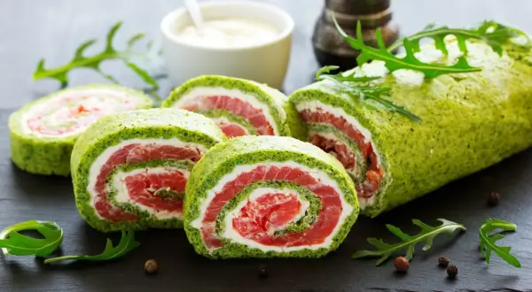 Rolada szpinakowa z mrożonego szpinaku z łososiem i serkiem, pokrojona w plastry, ozdobiona rukolą.
