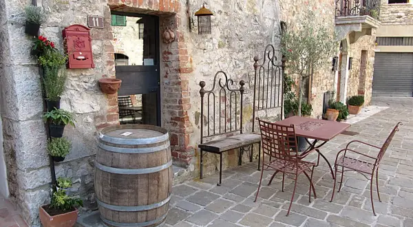 Un angolo pittoresco nella regione del Chianti con un barile di legno, piante aromatiche, un tavolino da esterno e un vecchio cancello in ferro battuto.