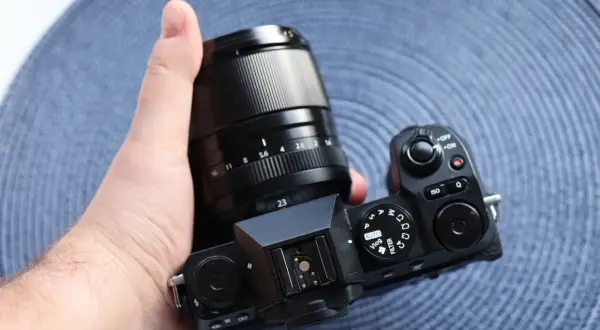 Dłoń trzyma aparat Fujifilm X-S20 z obiektywem. Widoczne pokrętła trybów i przyciski.