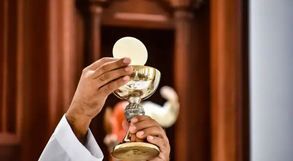 Kapłan w białej albie podnosi kielich z hostią, rozpoczynając liturgia eucharystyczna.