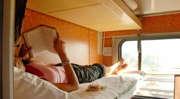 Frau liest Buch im Schlafwagen. Ein entspannter Urlaub im Zug mit Schlafwagen, die Landschaft zieht vorbei.