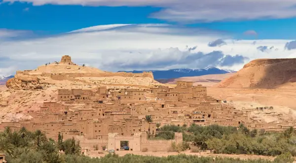 Ait Ben Haddou, en historisk befäst stad i Marocko, reser sig mot en blå himmel med moln.