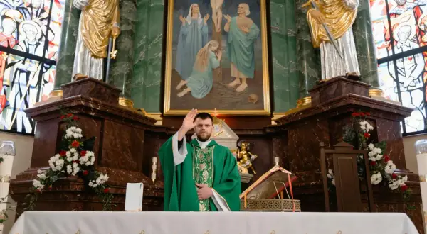 Ksiądz w zielonej szacie błogosławi wiernych. W tle obraz Jezusa na krzyżu. To moment święcenia wody w kościele.