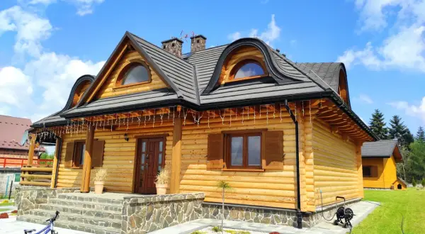 Drewniany dom z bali z kamiennymi schodami i rowerem na podjeździe.