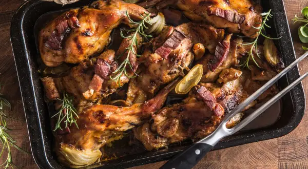 Coniglio panato al forno, dorato e succulento, con pancetta croccante, cipolle e rosmarino in una teglia.