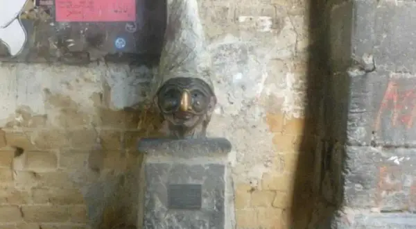 Busto con cappello a cono e un buffo naso di Pulcinella, su un piedistallo di pietra.