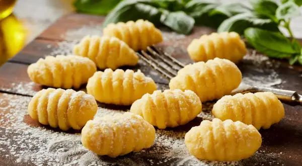 Świeżo przygotowane, puszyste makaron gnocchi, posypane mąką, leżą na drewnianej desce obok gałązek bazylii.