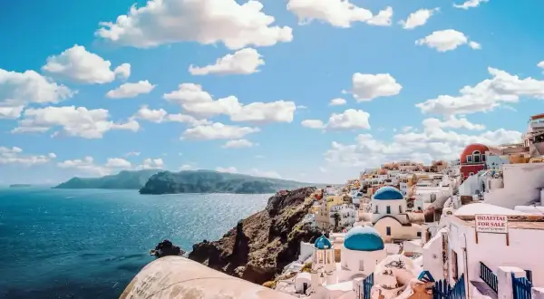 Widok na białe domy z niebieskimi kopułami na Santorini. Zastanawiasz się, ile się leci do Grecji, by podziwiać takie krajobrazy?