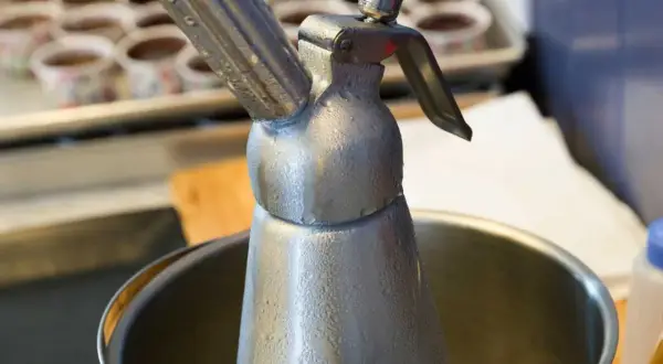 Metalowy syfon do bitej śmietany, pokryty kroplami kondensatu. Zastanawiasz się, ile może stać w lodówce?