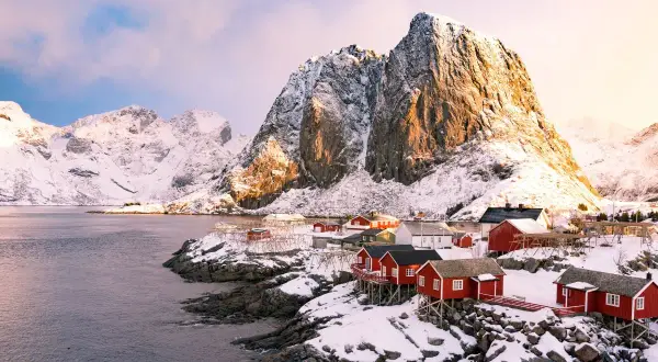 Village de pêcheurs aux maisons rouges sur pilotis, sous des montagnes enneigées. Un paysage typique de la Norvège.