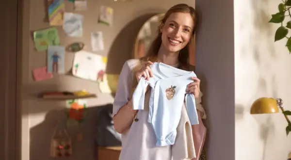 Glad mamma visar upp en ljusblå babybody med ett gulligt ekollonmotiv. Hon är veckans babe och ser fram emot att klä sin lilla skatt.