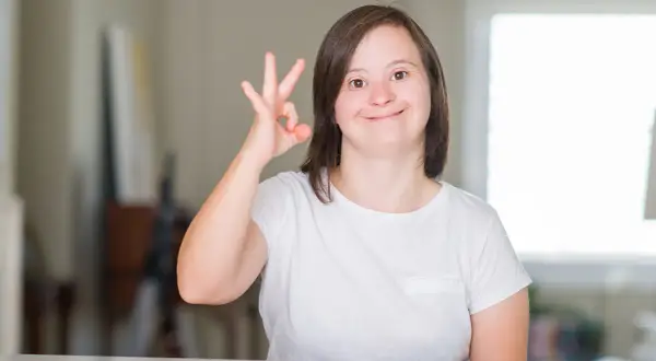 Ragazza con sindrome di down sorride e fa il segno "ok" con la mano.