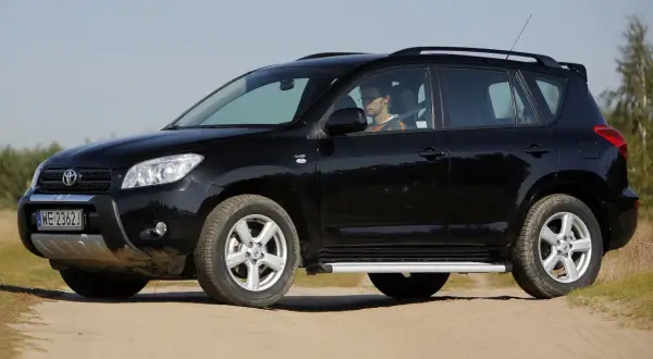 Czarny, mały SUV dla kobiety, zaparkowany na piaszczystej drodze. Kierowca w okularach siedzi za kierownicą.