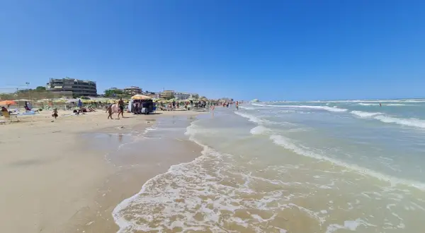 Spiaggia affollata a Senigallia mare, con ombrelloni, lettini, bancarelle e gente che passeggia. Il mare azzurro e calmo invita a un tuffo.