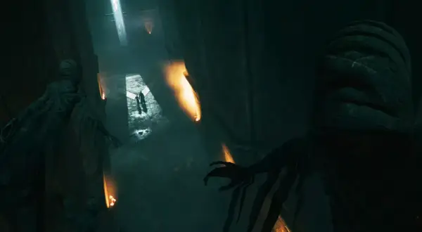 Dunkler Korridor in Hogwarts Legacy, der an Askaban erinnert. Mumienartige Gestalten lauern im Schatten, während zwei Figuren im Lichtschein voranschreiten.