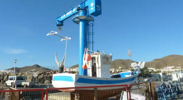 Barco pesquero blanco y azul en dique seco, bajo una grúa azul con "C.N. San José" escrito.