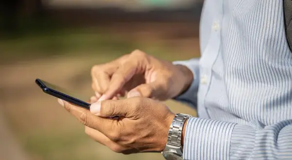 Mężczyzna w koszuli z paskami używa smartfona, szukając informacji, jak zamknąć konto Revolut.