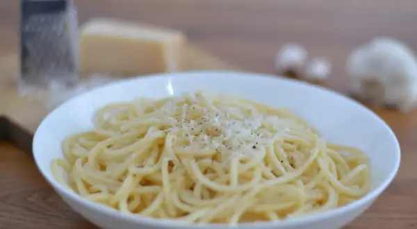 Ein Teller mit dampfenden Spaghetti, bestreut mit frisch geriebenem Parmesan. Dazu ein Stück Parmesan, eine Reibe und Knoblauch – perfekt für ein authentisches italienisches Gericht.