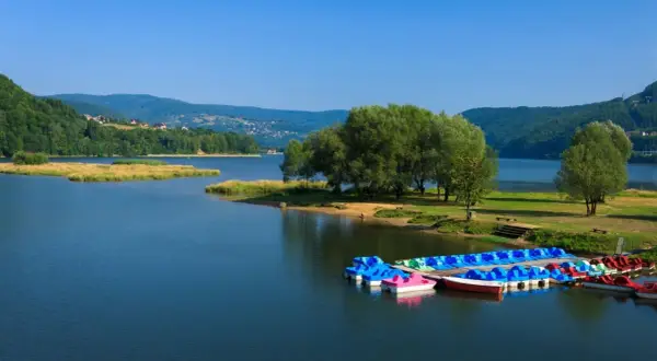 Jezioro Żywieckie, z kolorowymi rowerami wodnymi przy brzegu, otoczone zielonymi wzgórzami. Głębokość jeziora zachęca do wodnych zabaw.