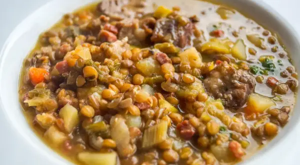 Un plato reconfortante de lentejas con trocitos de sobrasada, patatas y verduras en un caldo sabroso.