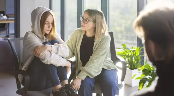 Wsparcie w trudnych chwilach: psychoterapia dla młodzieży. Dwie dziewczyny siedzą obok siebie, jedna z nich szuka pocieszenia.