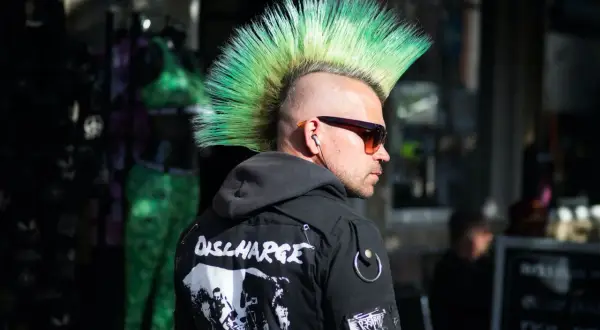 Mężczyzna z zielonym irokezem, w okularach przeciwsłonecznych i kurtce z naszywkami. Jego styl to czysty punk.