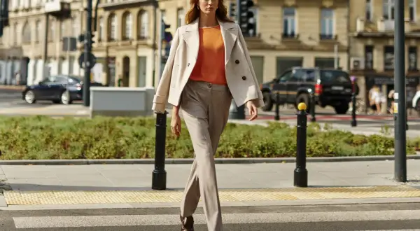 Elegancka kobieta prezentuje stylizacje do beżowego płaszcza, idąc przez pasy.