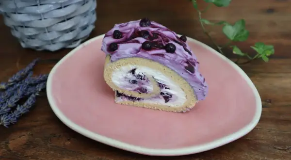 Roulé moelleux garni de crème chantilly mascarpone et myrtilles, nappé d'une crème violette aux fruits.
