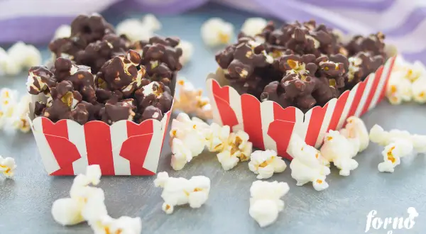Due contenitori a righe rosse e bianche pieni di pop corn al cioccolato, perfetti per scoprire come fare i pop corn al cioccolato.
