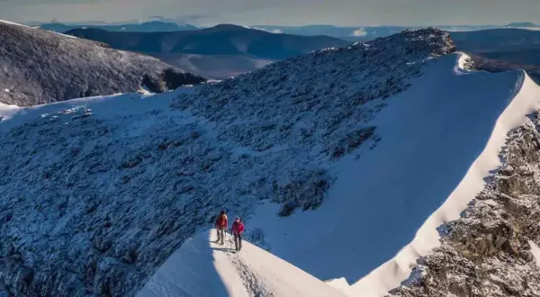 Två vandrare på en snöig bergskam med Kebnekaise i bakgrunden. En bra kebnekaise packlista är avgörande för en säker tur.