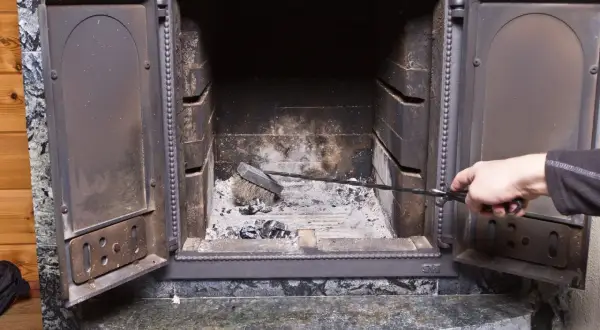 Maintenant, que faire de la suie de cheminée ? Une main utilise une pince pour nettoyer les cendres et la suie d'un foyer ouvert.