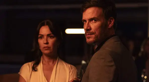 Man och kvinna i mörkt rum, en del av en psykologisk thriller topplista film. Mannen håller ett glas.