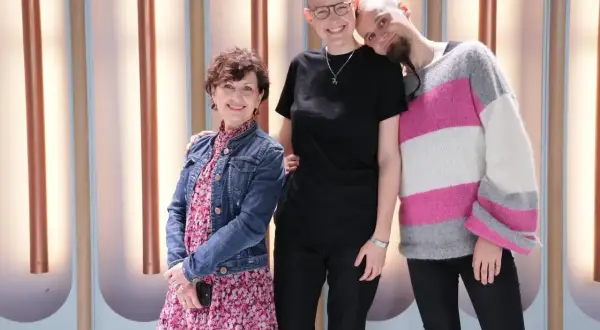 Osoba niebinarna co to znaczy? Trzy uśmiechnięte osoby stoją razem, jedna z nich ma krótkie włosy i okulary, druga z brodą i w swetrze w paski, a trzecia w sukience i jeansowej kurtce.