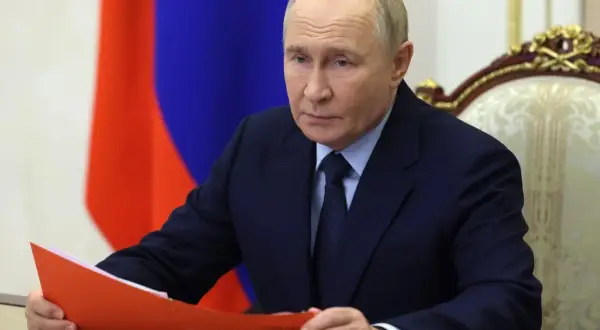 Władimir Putin w garniturze, z rosyjską flagą w tle, trzyma teczkę.