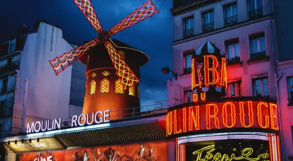 Le Moulin Rouge à Paris s'illumine la nuit, ses ailes de moulin rouge et jaune dansant sous le ciel sombre.