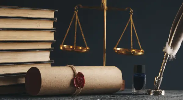 Waga sprawiedliwości, księgi i pieczęć na zwoju. Kto opłaca notariusza przy sprzedaży mieszkania? Zazwyczaj kupujący.