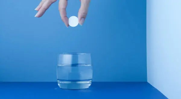Mano deja caer una pastilla blanca, como un micropur, en un vaso de agua.