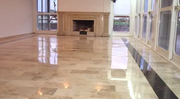 Pavimento in travertino lucidato a specchio, con un camino in marmo e grandi vetrate che riflettono la luce.