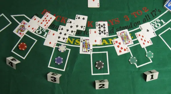 Stół do gry w blackjacka z kartami, żetonami i kostkami. Gra toczy się o wysokie stawki.