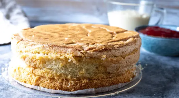 En gyllene tårtbotten, redo för ett tårtbotten recept. Bredvid står en skål med sylt och en kanna med grädde.