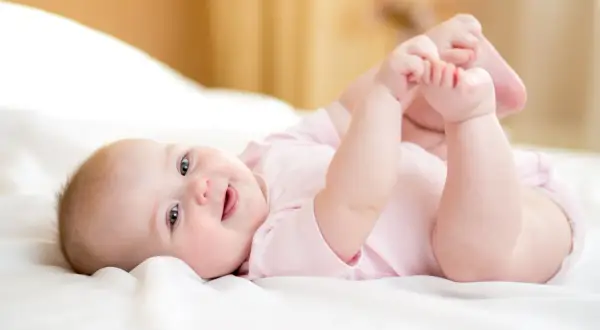 Ein fröhliches Baby von 8 Wochen liegt auf dem Rücken und spielt mit seinen Füßen.