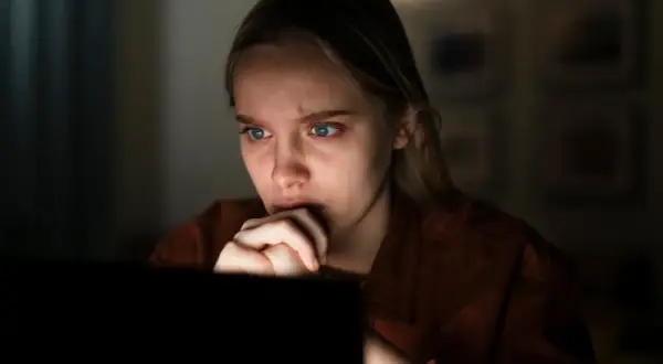 Przerażona dziewczyna wpatruje się w ekran, czując się jak ofiara stalkingu.