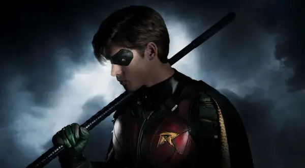 Robin z obsady Titans, z maską na oczach i kostiumem z symbolem R, trzyma pałkę.