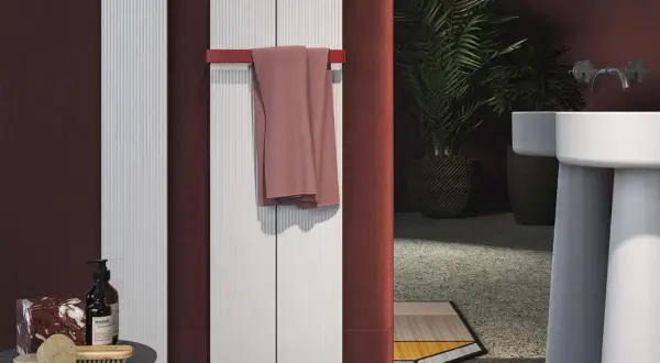 Termosifoni elettrici: pro e contro. Due radiatori bianchi verticali con un asciugamano rosa appeso. Un bagno moderno con piante e lavabo.