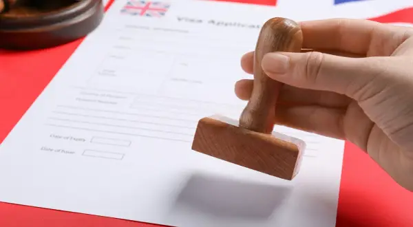 Dłoń trzyma pieczątkę nad formularzem wniosku o wizę do Anglii.