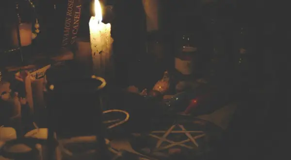 Mroczna atmosfera, płonąca świeca, książka z napisem "Cinnamon Rose", muszelki i pentagram. Czy pentagram jest zły? To zależy od intencji.