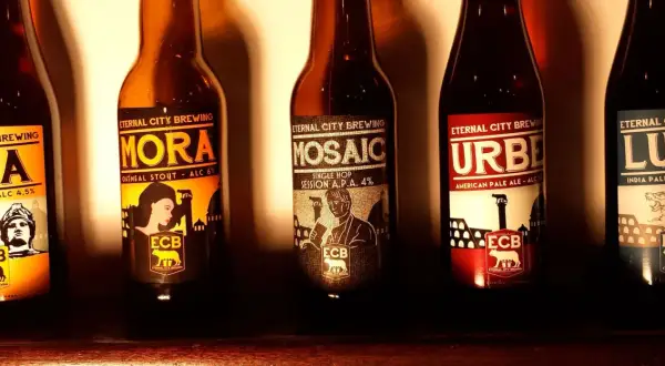 Cinque bottiglie di birra artigianale di Eternal City Brewing, con etichette raffiguranti monumenti e figure iconiche.
