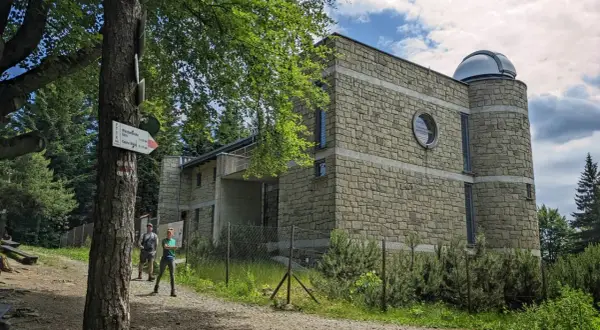 Kamienny budynek obserwatorium astronomicznego na szczycie góry. Obok tabliczka szlaku turystycznego PTTK.
