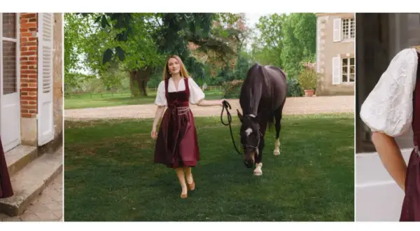 Eine Frau in einem weinroten Dirndl mit einer glänzenden Dirndlschürze aus Seide, daneben ein Pferd auf einer grünen Wiese.